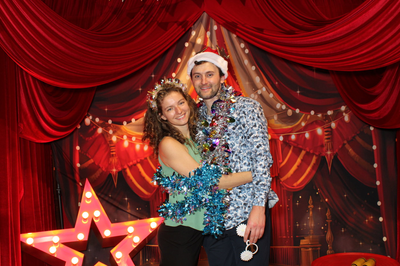 Two PwC colleagues in a Santa hat and tinsel next to a lit-up marquee star
