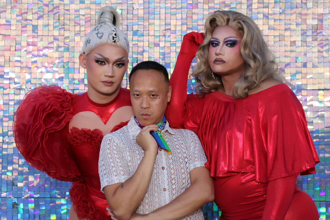 Two drag queens in red posing with a guest at the Rethink Pride Party photo booth