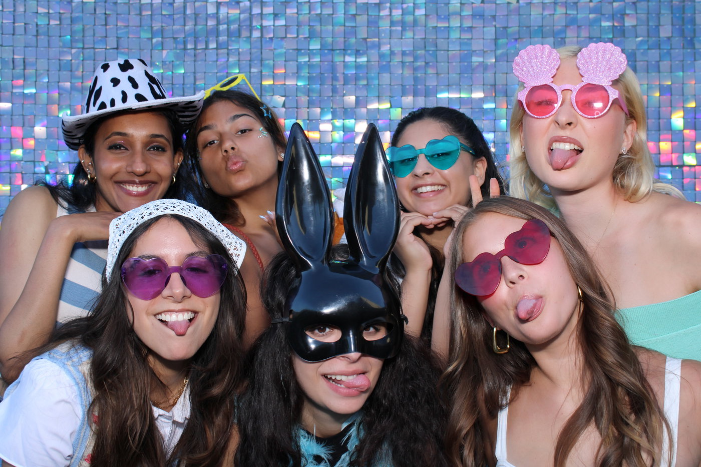 Friends in party glasses, a bunny mask and hats on a holographic shimmer wall at the Rethink Pride Party