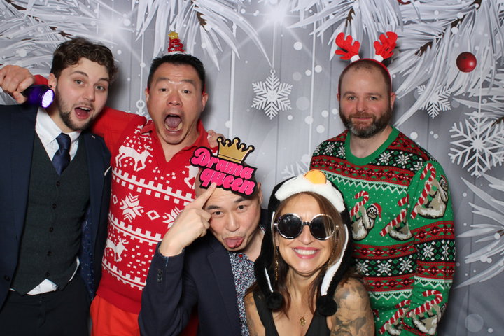 Coworkers in ugly Christmas sweaters on a silver snowflake backdrop