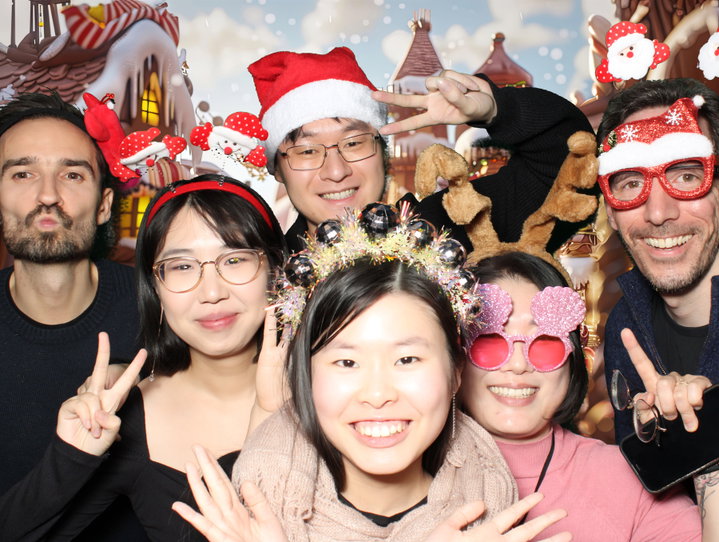 Coworkers in festive glasses in front of a gingerbread village