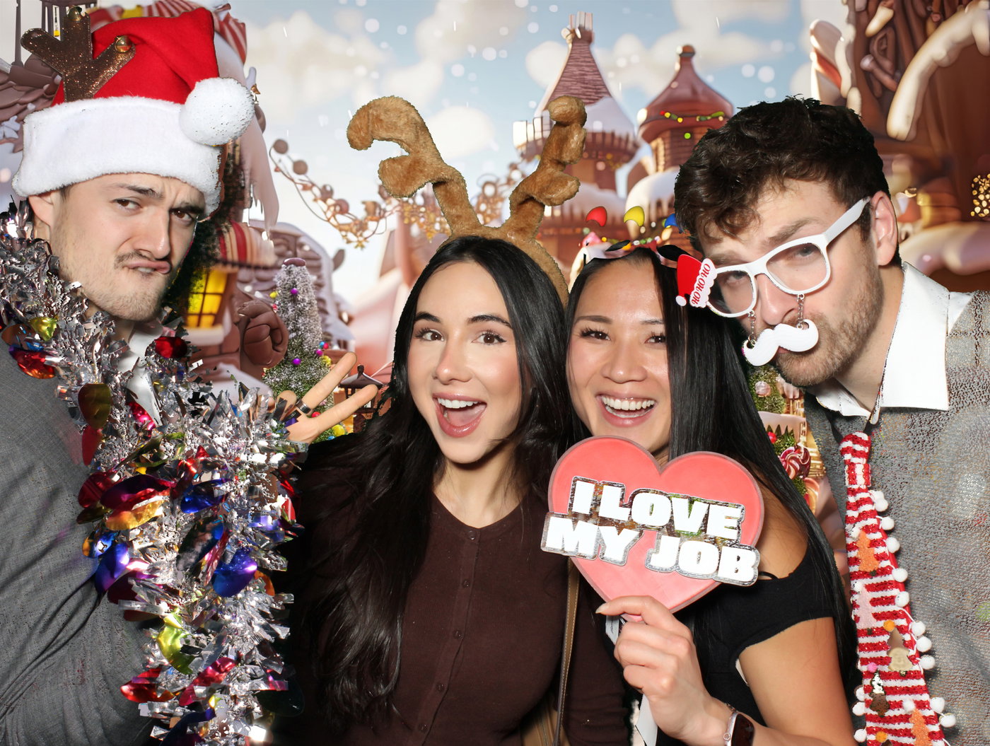 Planview colleagues with tinsel, antlers and an I love my job sign in front of a gingerbread village